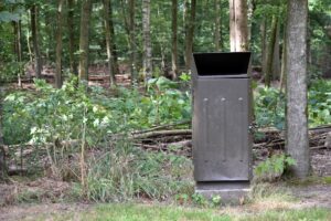 A person fastening a secure, animal-resistant trash bin outside a suburban home on a clear morning.